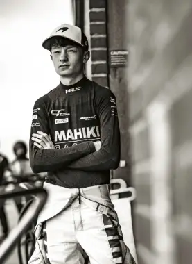 Revie Lake in Mahiki Racing overalls and a team cap, arms folded in the paddock