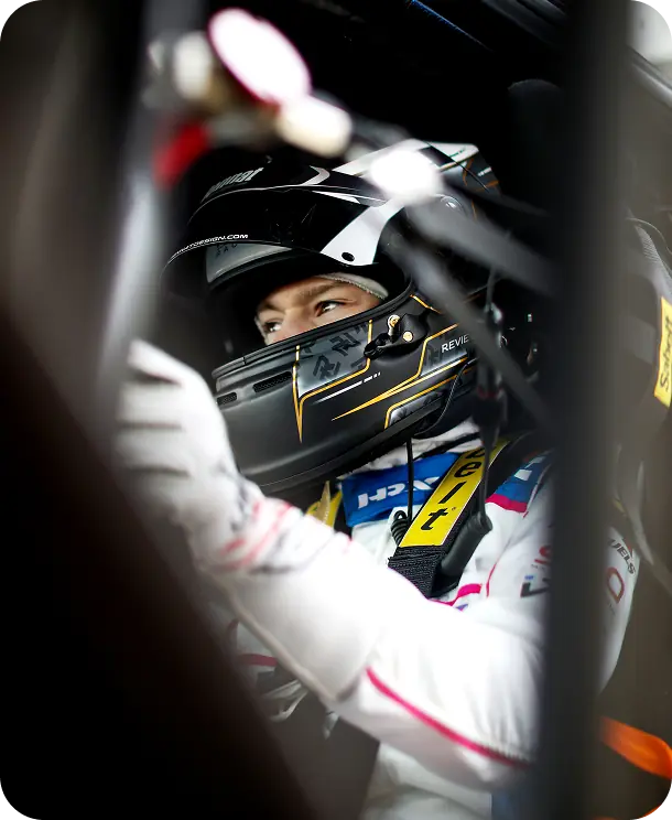 Revie Lake helmeted in the cockpit, hands on the wheel, seen through the car's window