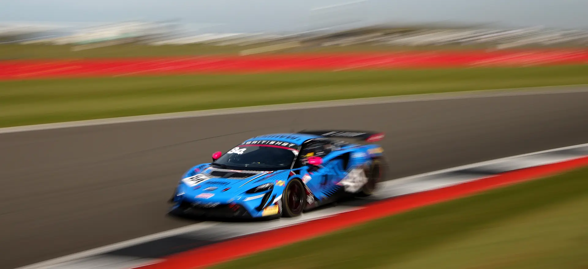 The number 84 Mahiki Racing McLaren Artura GT4 at speed past the Silverstone kerbs
