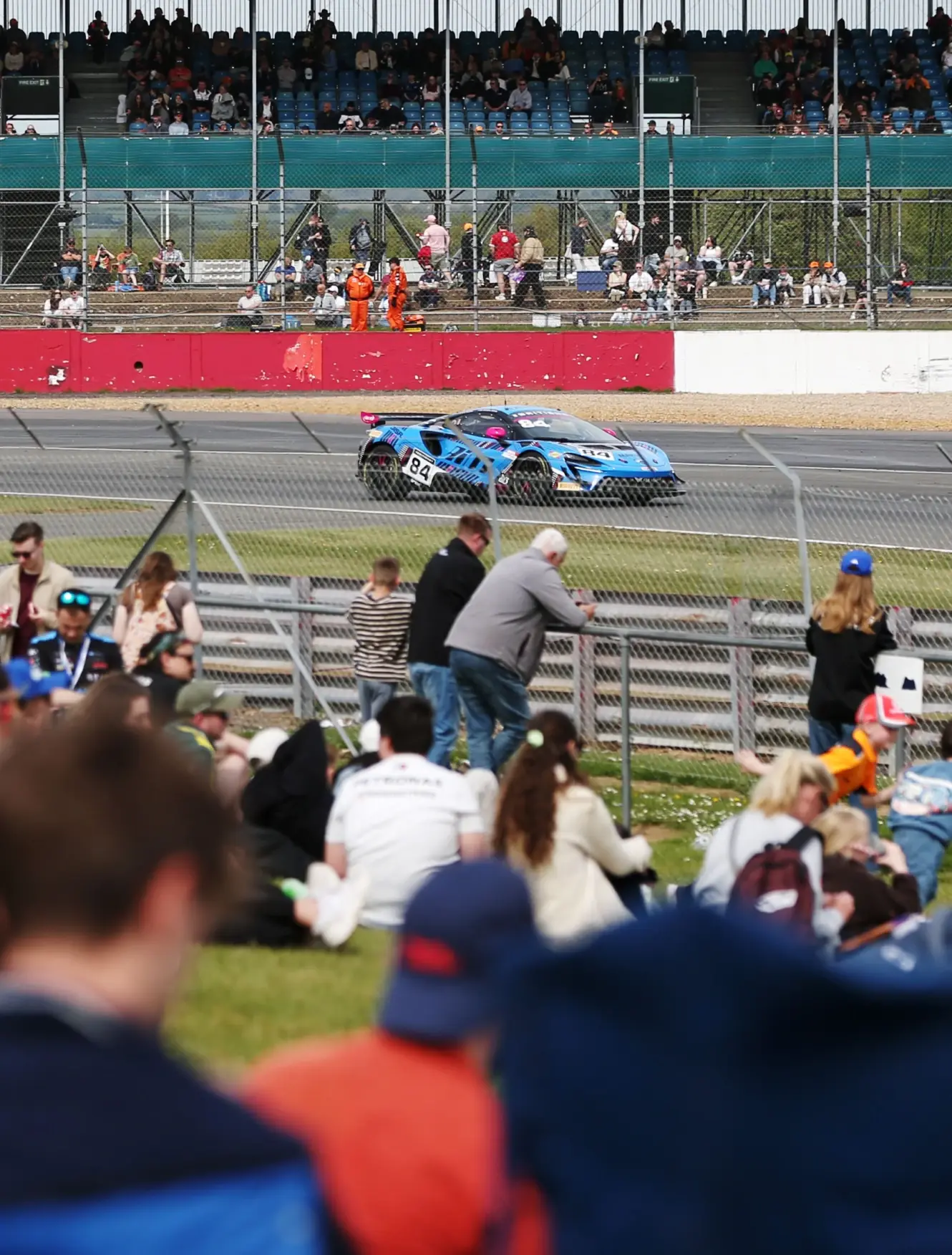 Spectators on the grass bank watching the number 84 car pass at Silverstone