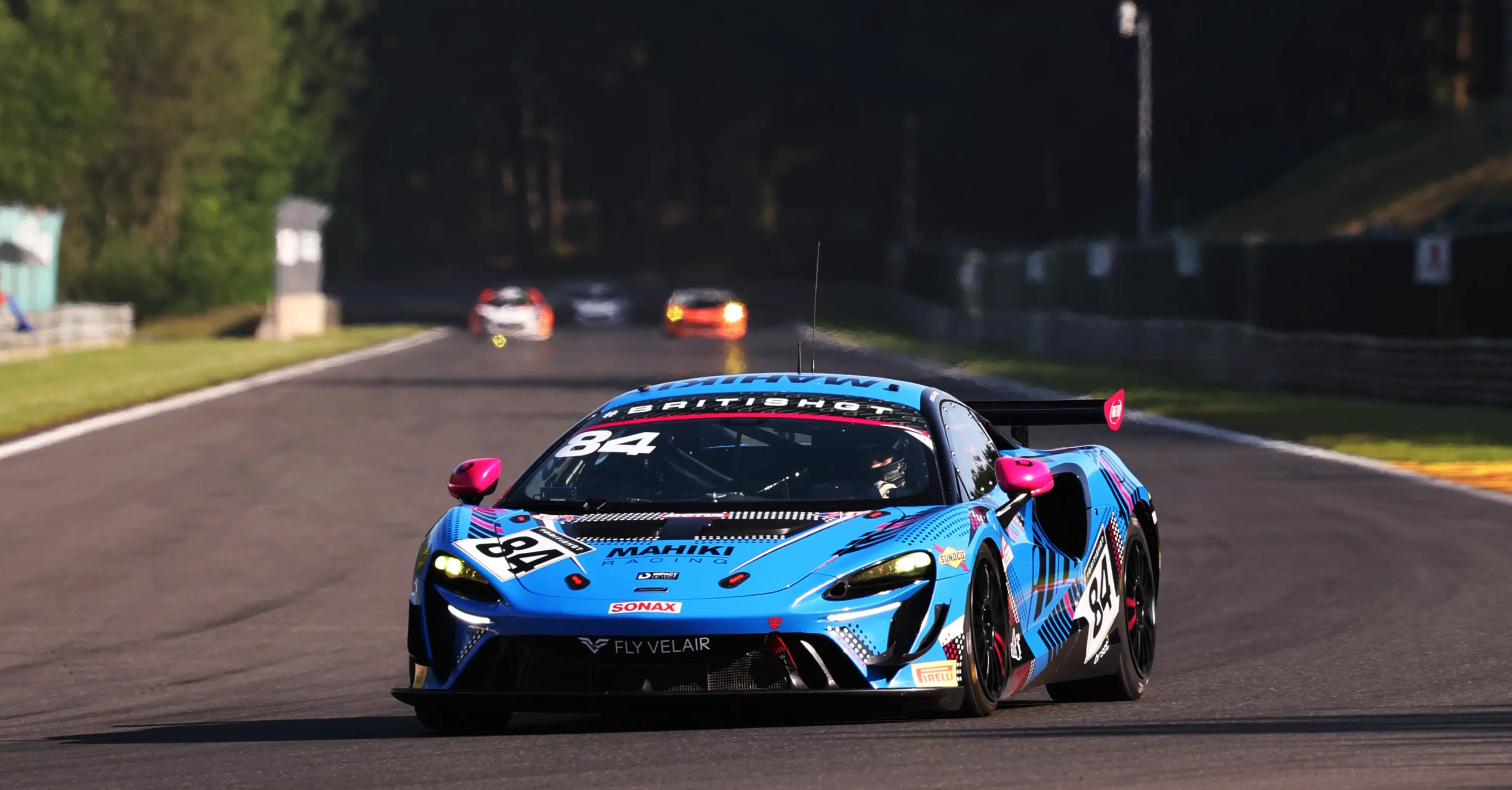 The number 84 Mahiki Racing McLaren Artura GT4 panning past the Silverstone Wing pit building