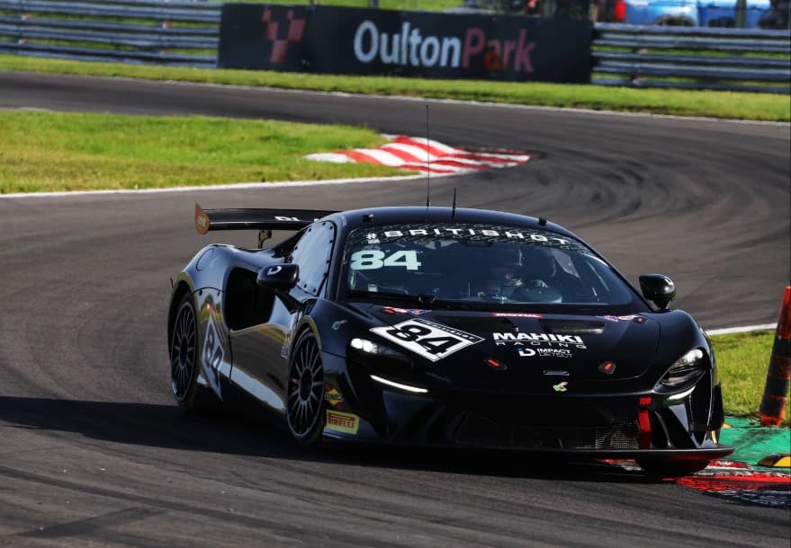 The black number 84 Mahiki Racing McLaren Artura GT4 passing the Oulton Park trackside signage