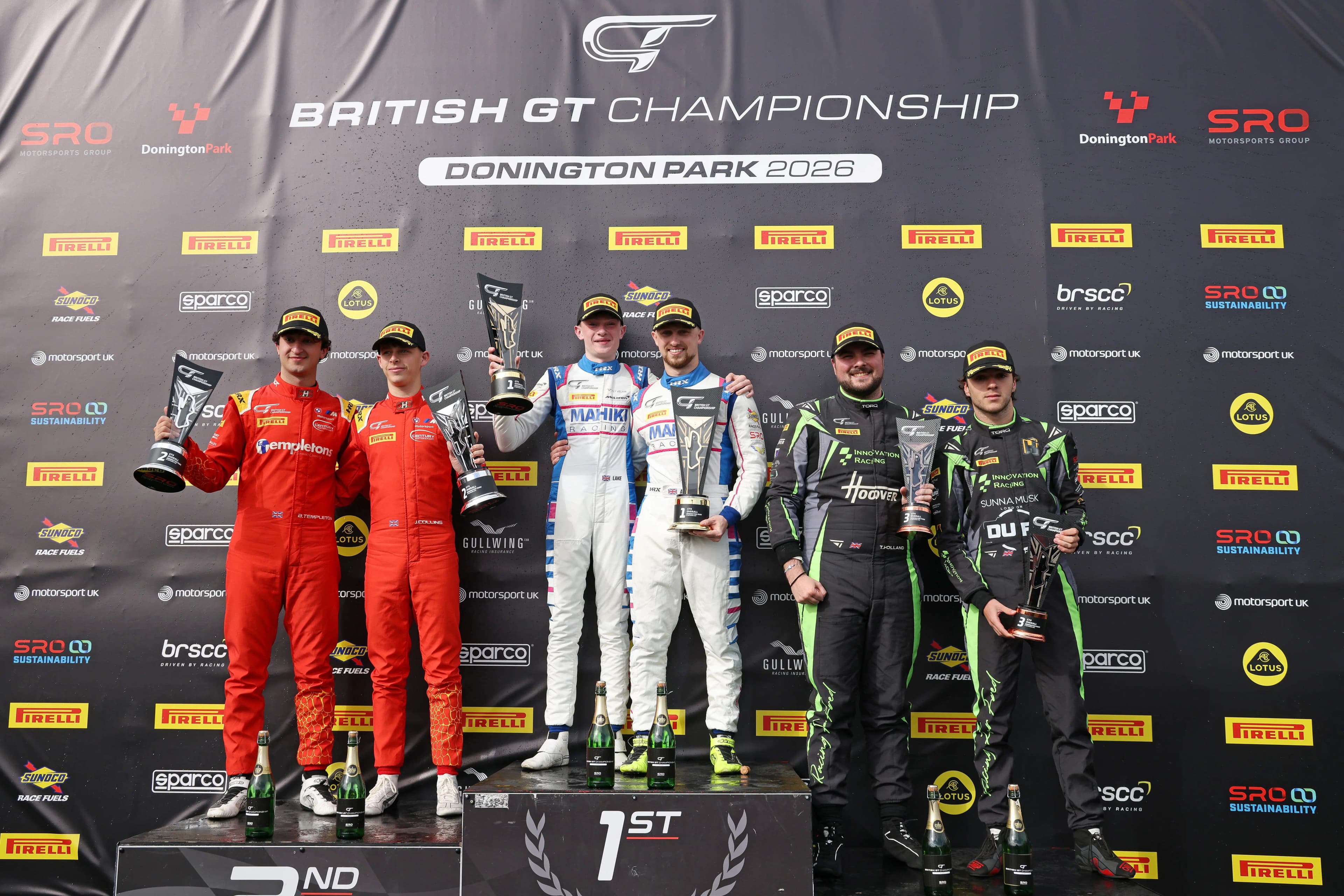Revie Lake and Blake Angliss on the top step of the GT4 podium at Donington Park, holding their winners' trophies alongside the second and third-placed crews
