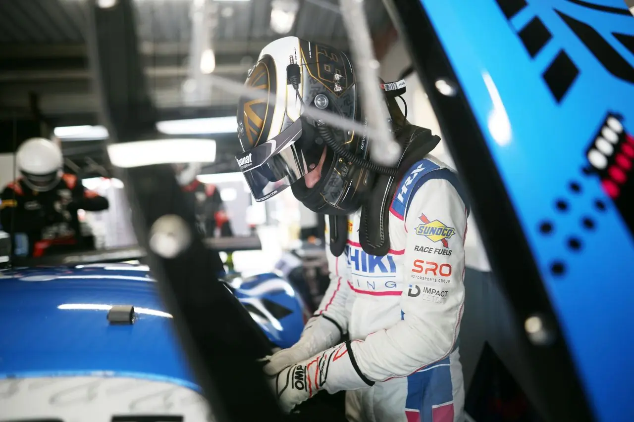 Revie Lake, helmeted and connected to the radio, leaning into the number 84 McLaren Artura GT4 in the garage